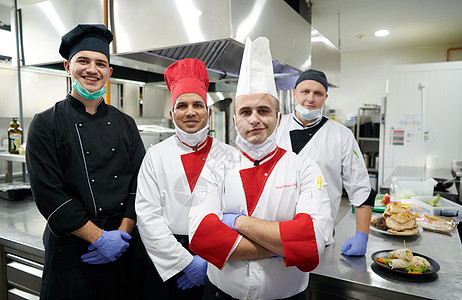 在冠状病毒新常态概念下 一群厨师戴着防护医用口罩和手套站在餐厅的厨房里团体混血帽子食物感染保健美食卫生工作男性图片