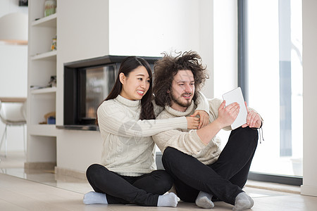 在壁炉前使用平板电脑的多种族夫妇在壁炉前成人微笑男人互联网女孩奢华头发网络夫妻女士背景图片