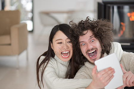 在壁炉前使用平板电脑的多种族夫妇在壁炉前网络男人奢华成人地面女士微笑思考冲浪生活背景图片