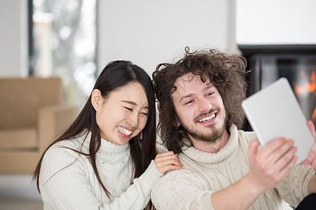 在壁炉前使用平板电脑的多种族夫妇在壁炉前女孩微笑互联网女性女士头发冲浪奢华生活男人背景图片