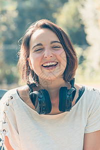 短发的年轻女性在使用大耳机 耳机 在外面听音乐 休闲概念 轻松的假期时笑图片