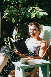 在阳光明媚的一天 在椅子上靠背 复制空间 放松和爱好概念时 持有一本看得严肃到照相机面前的书籍的妇女图片