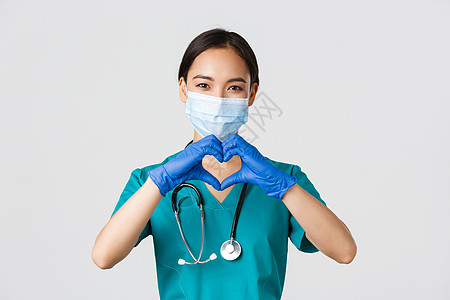 Covid19 冠状病毒病 医护人员的概念 迷人微笑的亚洲女医生 戴医用面具和橡胶手套的医生的特写 为病人提供护理 展示心形护士图片