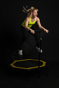 穿着黄色 T 恤蹦床的黑色背景健身蹦床上的女孩适合活跃的身体健康运动 可爱的俱乐部 人白教练 身体肌肉教练享受图片
