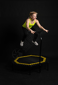 身穿黄色 T 恤的黑色健身女健身蹦床上的女孩 运动型生活方式的有氧运动 体重弹跳 迷你健美操 年轻肌肉教练尽享背景图片