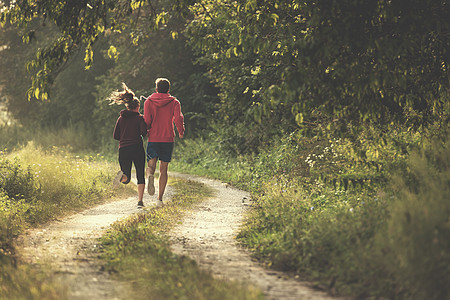 在乡村公路上慢跑的年轻夫妇阳光运动跑步运动装女士训练国家慢跑者享受森林图片