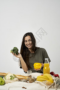 穿着绿色 T 恤的快乐女人打开购物网眼生态袋 里面装着健康的素食蔬菜 水果 面包 零食 手里拿着西兰花和黄胡椒 健康饮食素食的概图片