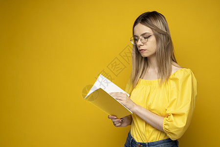 美丽聪明的年轻女孩拿着和阅读孤立在黄色背景上的书 穿着黄色衬衫 戴着眼镜看书的漂亮女人的画像 教育 学习 知识女士闲暇微笑女性青图片