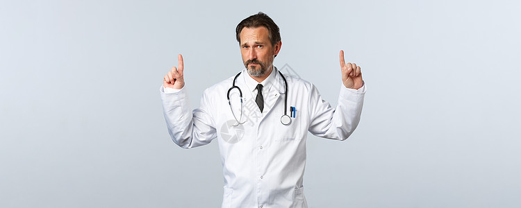 Covid19 冠状病毒爆发 医护人员和流行病概念 持怀疑态度的成年男医生身穿白大褂 手指向上 看着镜头 心存疑虑擦洗护理疫苗科图片