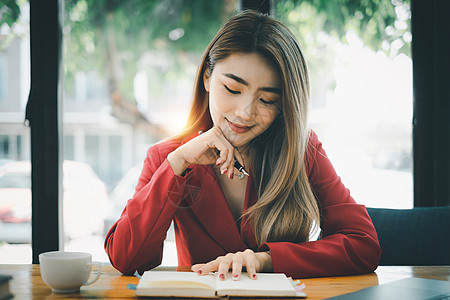 亚洲商业女商务人士在笔记本上用笔笔写演讲稿 她手里拿着一支笔 咖啡店的理念放宽时间图片