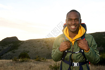 带着背背包微笑和背景中日出的笑容的年轻非洲男子图片