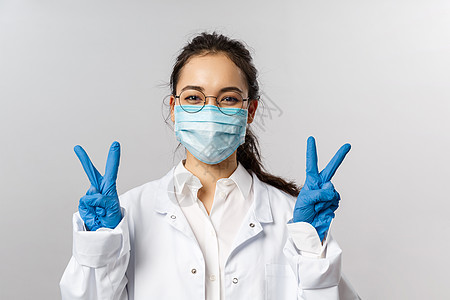 Covid19 冠状病毒 医疗保健和医生的概念 乐观的亚洲女医生画像要求保持安全 戴上医用口罩和手套 展示和平标志 希望我们战胜图片