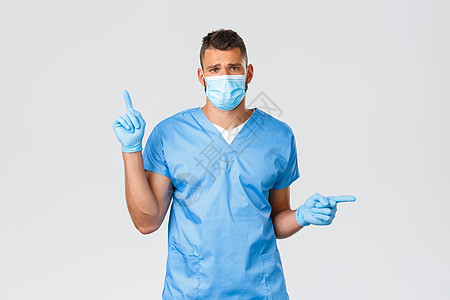 医护人员 covid-19 冠状病毒和病毒概念 悲伤而疲惫的医生 穿着磨砂膏的西班牙裔男护士 医疗面罩和手套指向侧面 在夜班时感图片