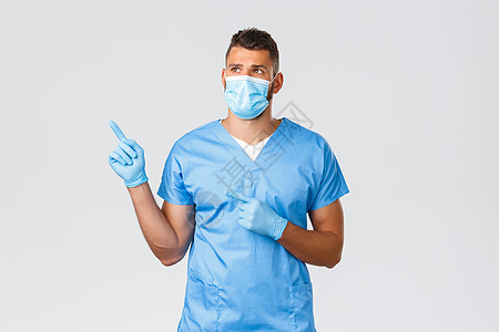 医护人员 covid-19 冠状病毒和预防病毒的概念 身着蓝色磨砂服的年轻帅气医生 戴着医用口罩和手套的男护士 向左指指点点 阅图片