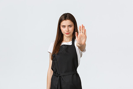 杂货店员工 小型企业和咖啡店的概念 严肃坚定的女咖啡师伸出手说停止 限制或禁止行动 站在黑色围裙中图片