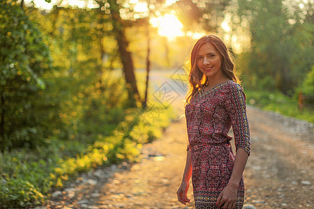 年轻女子穿着衣服 走在森林道路上 背景中有金色的夕阳光图片