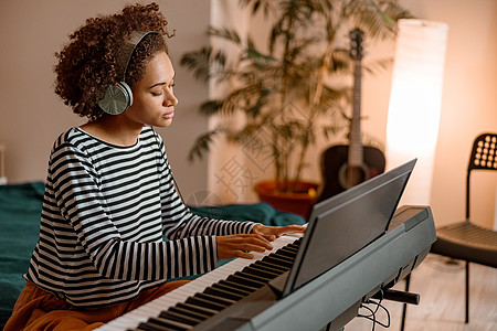 耳机中的年轻女青年在家玩合成器闲暇钢琴艺术家钥匙玩家音乐家乐器成人卧室爱好图片