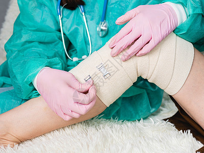 一名身戴医疗手套的医生在病人腿部和膝盖上贴有弹性绷带 伤病学家对病人施用弹性材料以及诊所医院医师创伤韧带扭伤外科伤害松紧带援助图片