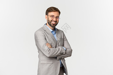 充满自信的商务人士长胡子 穿灰色西装和眼镜 胸前交叉手臂 微笑自我保证 站在白色背景之上的肖像喜悦套装情感商业广告职业金融工作室图片