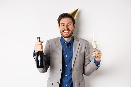 欢庆和节假日概念 有趣的醉醉酒者穿西装 戴生日帽子 瞪眼 在派对上玩得开心 喝香槟 喝白背景成功生活快乐经理套装假期庆典人士工作图片