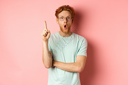 迷人的年轻红头发男子 用乌瑞卡手势举起手指和投出想法 站在粉红色背景上男性微笑解决方案购物促销红色粉色广告胡子成人图片