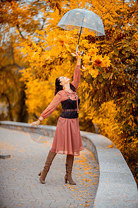 秋天公园穿着带雨伞的漂亮女孩 她把他抱在头顶上 秋叶从他身上掉出来天气公园城市树叶乐趣森林黑发衣服外套成人图片