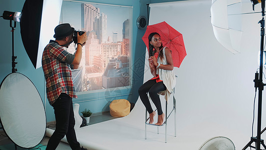 现代时尚杂志摄影照片拍摄的非洲时装模特 在酒吧高椅子上配着红色雨伞图片