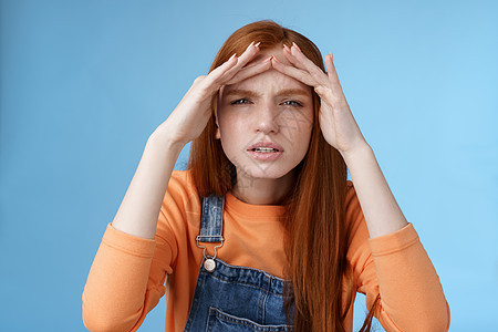 迷惑不解的可爱风趣的红头发欧洲女人正在寻找眯着眼睛的人 如果没有眼镜 就无法看到远处 手握着前额遮住视线 站在蓝色背景中青少年女图片