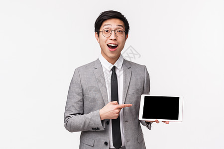 身穿灰色西装 兴奋 热情的亚洲帅哥的腰上画像描述了他公司的巨额收入 在数字平板电脑显示屏上展示图表 站在白色背景上图片
