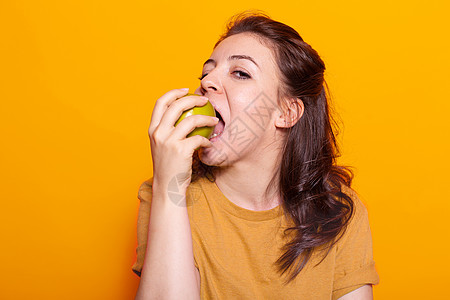 健康女性在相机上咬绿苹果的肖像图片