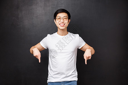 身穿白色 T 恤的快乐英俊亚洲男学生的工作室肖像 邀请新成员加入他的团队开始职业生涯 指指点点看这里的标志 微笑的相机图片