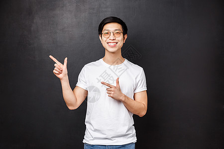 帅气的亚洲年轻男子的肖像 身穿白衬衫的男学生在促销 折扣优惠或横幅上指着左上角 微笑的相机 建议访问链接 黑色背景图片