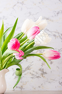 一束白色和粉红色的郁金香花 有绿叶 放在桌子上的一个罐子里 垂直视图图片