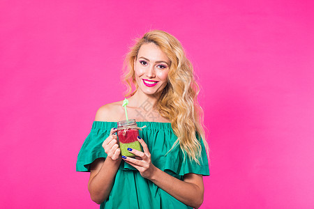微笑着的年轻女子在粉红背景上 喝清冰汁的肖像玻璃稻草水果蔬菜果汁头发女性帽子饮料工作室图片