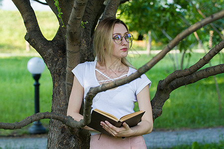 迷人的年轻姑娘 在公园里手握一本书 在树枝上靠着一棵树枝图片