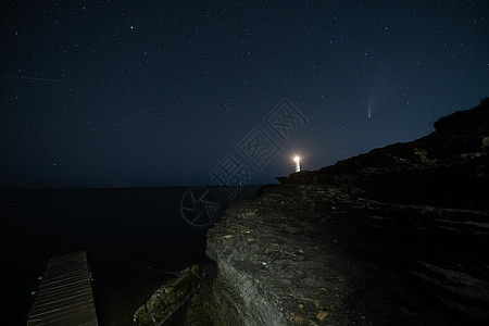 在海滩的夜空中 白色灯塔上空的新颖彗星的风景图片