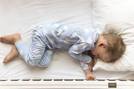 顶视图 可爱的小 23 岁学龄前男婴孩子在午餐休息时间穿着蓝色睡衣在家里用枕头甜甜地睡在白色婴儿床里 童年 休闲 舒适 医药 健图片