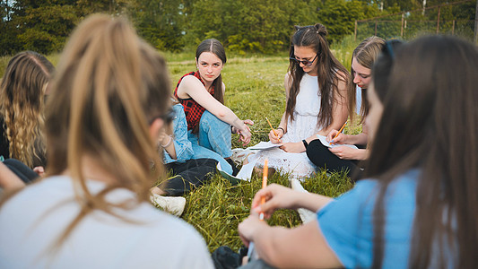 一群女学生坐在草地上的圆圈里 用笔记本进行集体工作男孩们成年人童年学习女孩们班级快乐老师公园团体图片