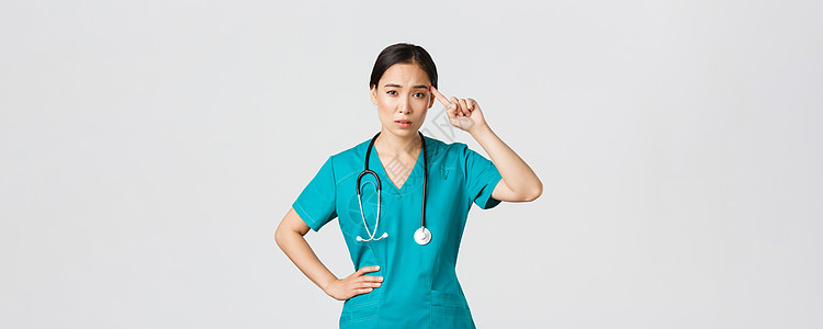 Covid19 医护人员 流行病概念 恼怒 持怀疑态度的亚洲女护士或医生责骂那些表现得疯狂或愚蠢的人 用评判的脸在太阳穴上滚动手图片