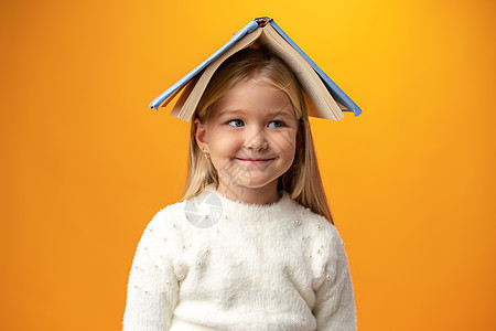小姑娘头上拿着书 看着黄色背景的照相机 看黄底的背景幼儿园工作室教育文学学生学校阅读家庭作业学习孩子们图片