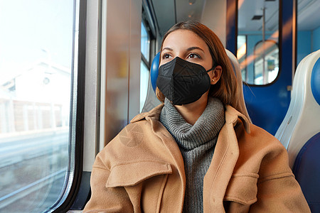 年轻体贴的女人戴着黑色医用口罩在火车上透过窗户往外看 大流行期间旅行和使用公共交通工具的概念图片