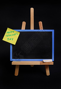 教师节模板木桌画架的特写 带粉笔和黑板 空白处为文本 粘贴便条纸 题词为教师节 黑色背景与复制空间隔离背景