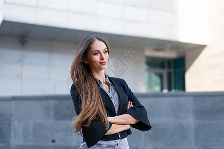 身穿黑色夹克 长发的女商务人士站在户外 靠近公司办公楼 双手合十职业商务经理商业企业家折叠黑发员工套装城市图片