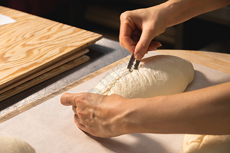 在烤箱中烘烤之前 面包师的女手用刀片将一条面团切成一条面包的特写镜头 工艺面包制作工人制造业店铺商业包子工作生产面粉工厂切口图片