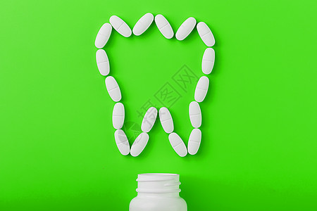 在绿色背景的白色罐子上洒出的牙齿 以维生素钙的形式呈现出来处方制药剂量矿物质胶囊医院维生素化学品抗生素药物图片