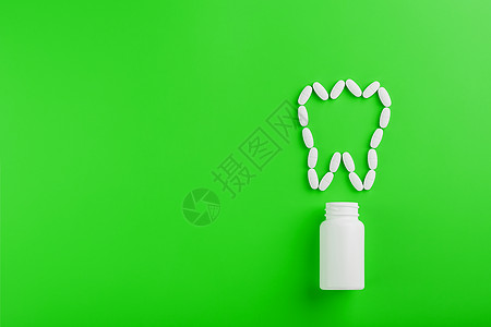在绿色背景的白色罐子上洒出的牙齿 以维生素钙的形式呈现出来剂量医生医院治疗止痛药丸药制药蓝色胶囊矿物质图片