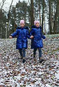 两个双胞胎女孩跑下山坡 被第一场雪覆盖喜悦土地幸福快乐乐趣女朋友享受叶子家庭跑步背景图片