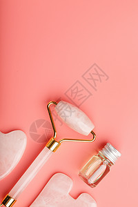 一套面部按摩技术工具 由粉红色背景的天然玫瑰石英制成 在玻璃罐中用滚筒 玉石和油进行脸部和身体护理平铺穴位宝石魅力女性按摩器瓜萨图片