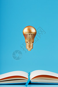 一个金色灯泡悬挂在蓝色背景笔记本的空白页上方力量解决方案智力创造力记事本头脑领导清洁度悬浮想像力图片