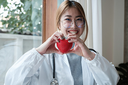 年轻年轻的亚洲美丽的医生 听诊器握着心 站在她的办公室里 笑声有氧运动考试核弹男人诊所女士治疗医院手术身体图片